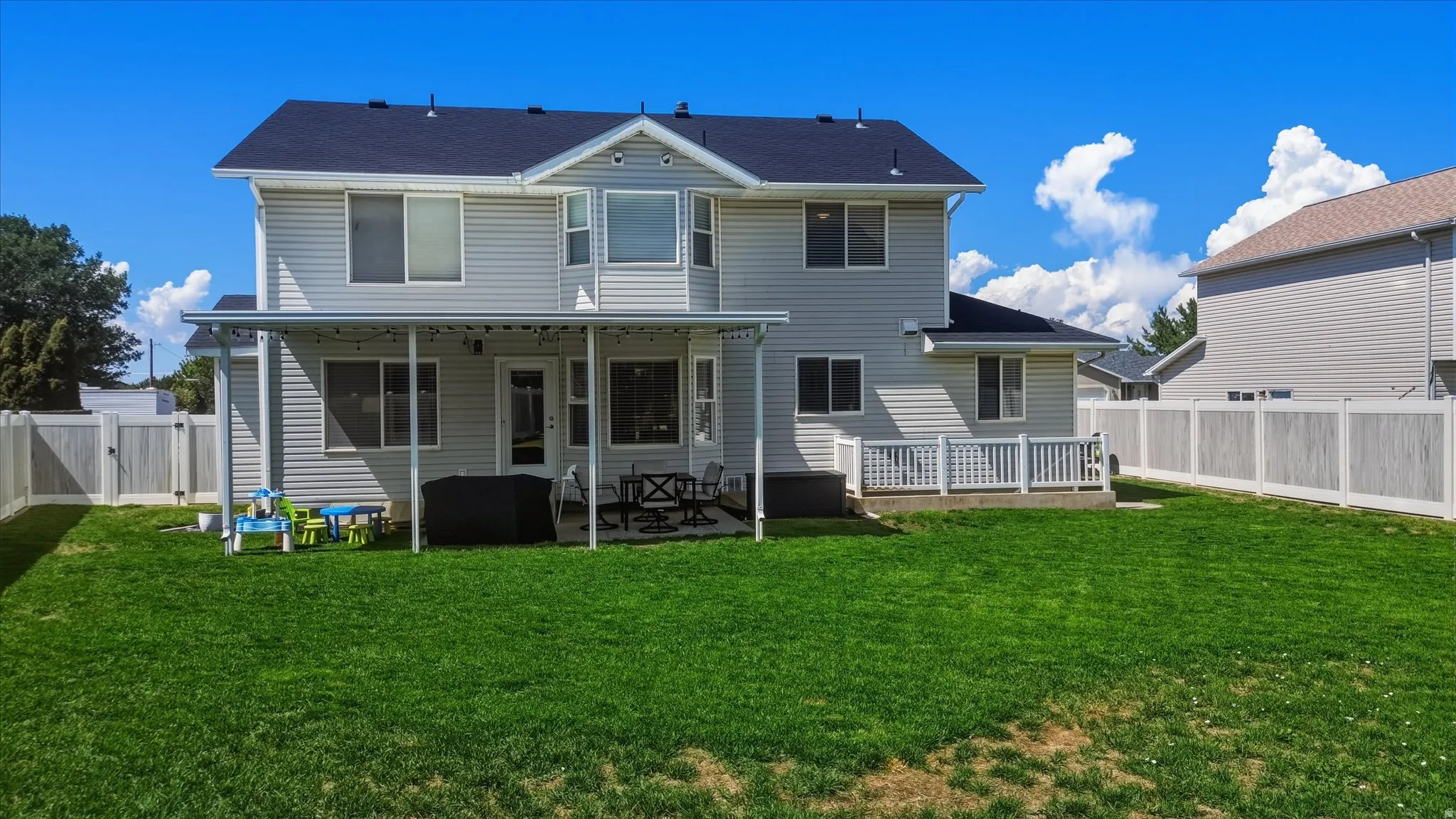 Expansive green lawn with a full vinyl fence and a covered patio