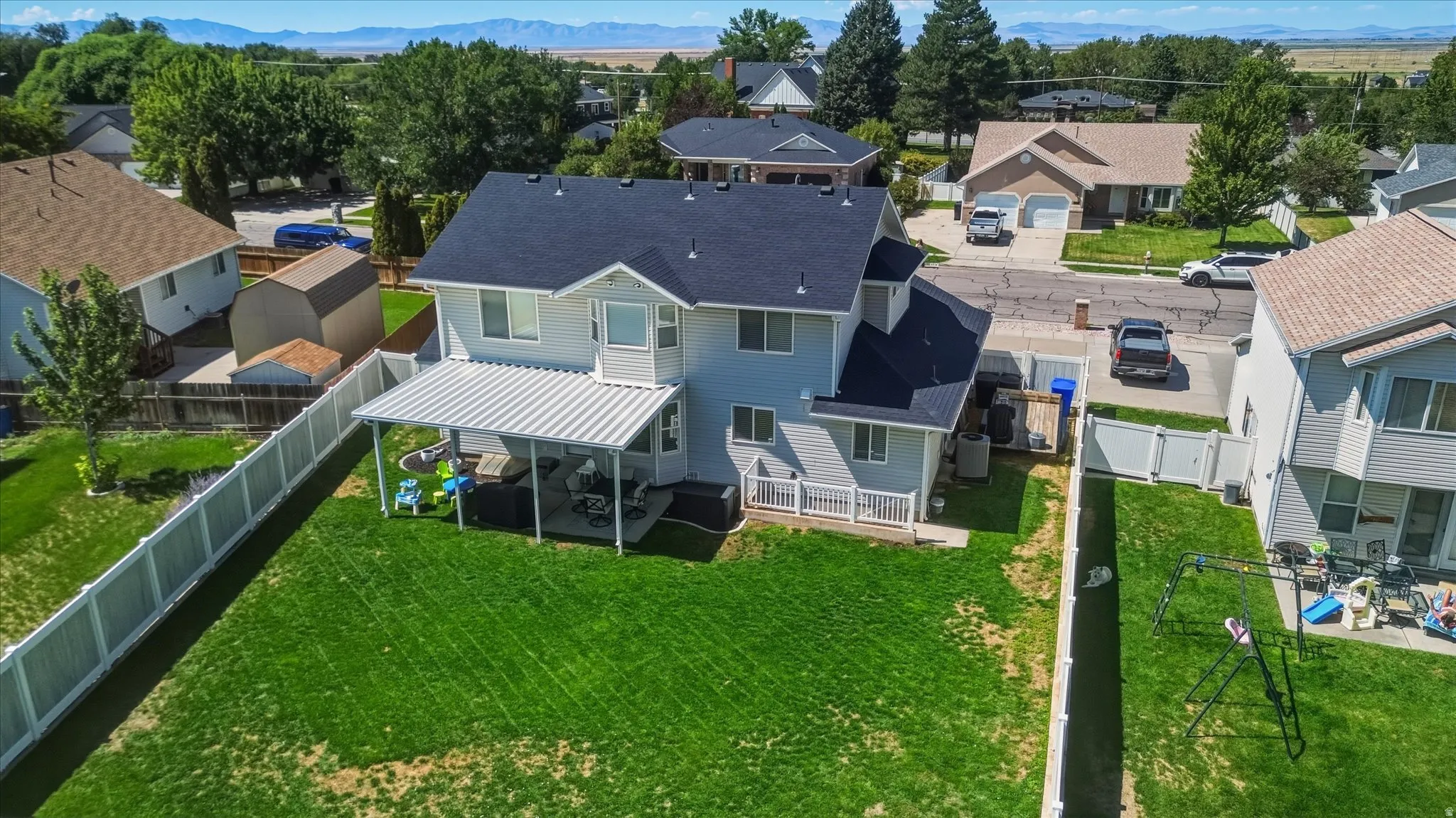 Expansive green lawn, white privacy fencing, covered patio structure, rear deck, and a shed