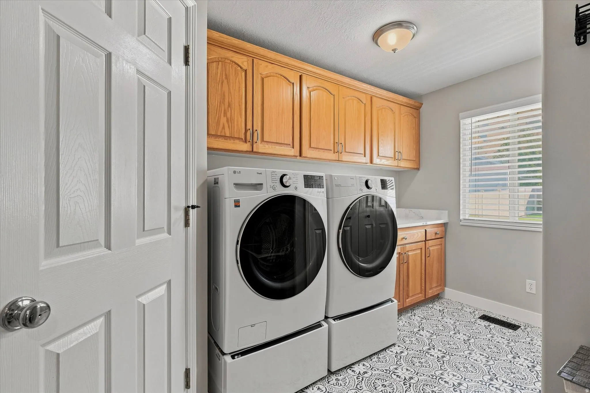 Laundry area featuring wood cabinetry, patterned floor tiles, a window with blinds, and a flush-mount ceiling light