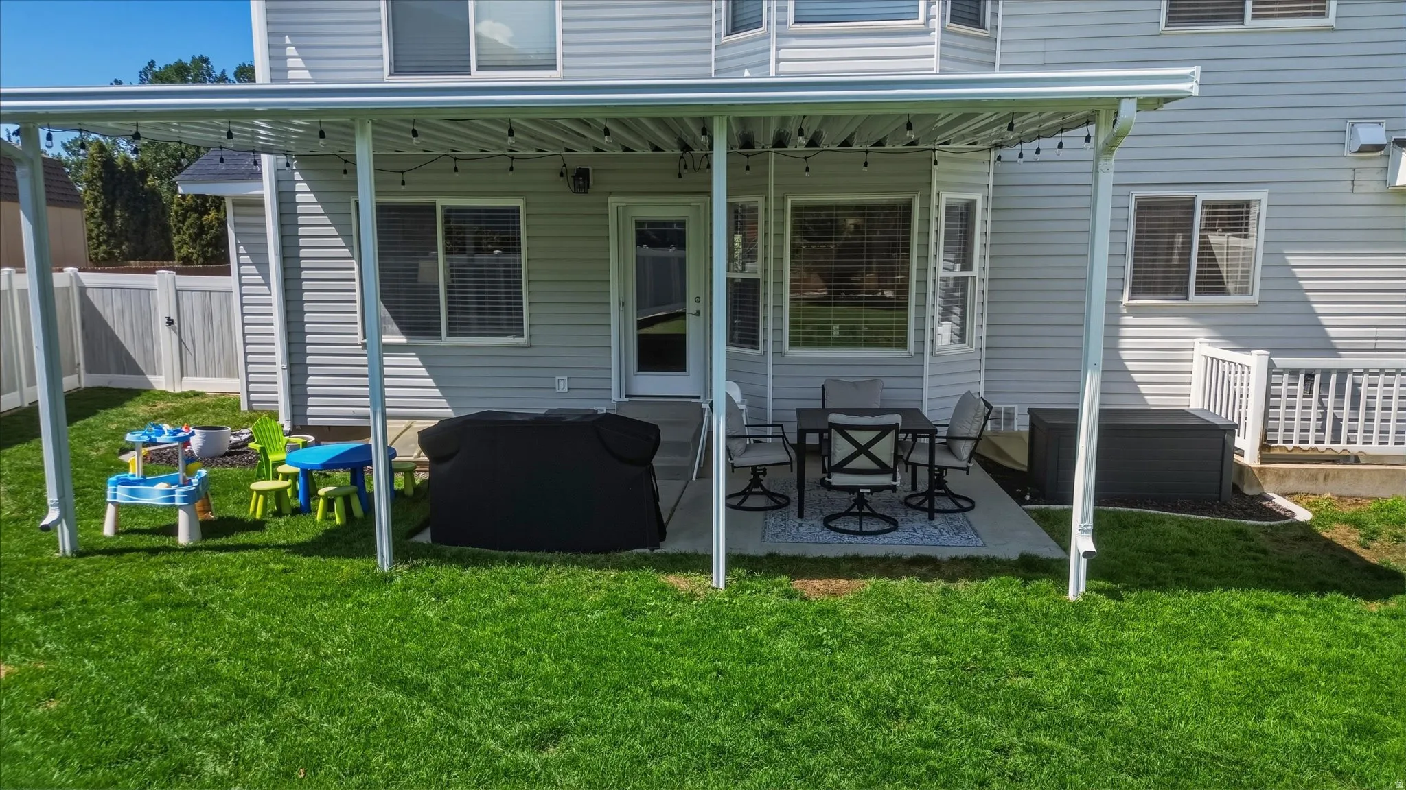 Lush green lawn with a covered patio featuring string lights