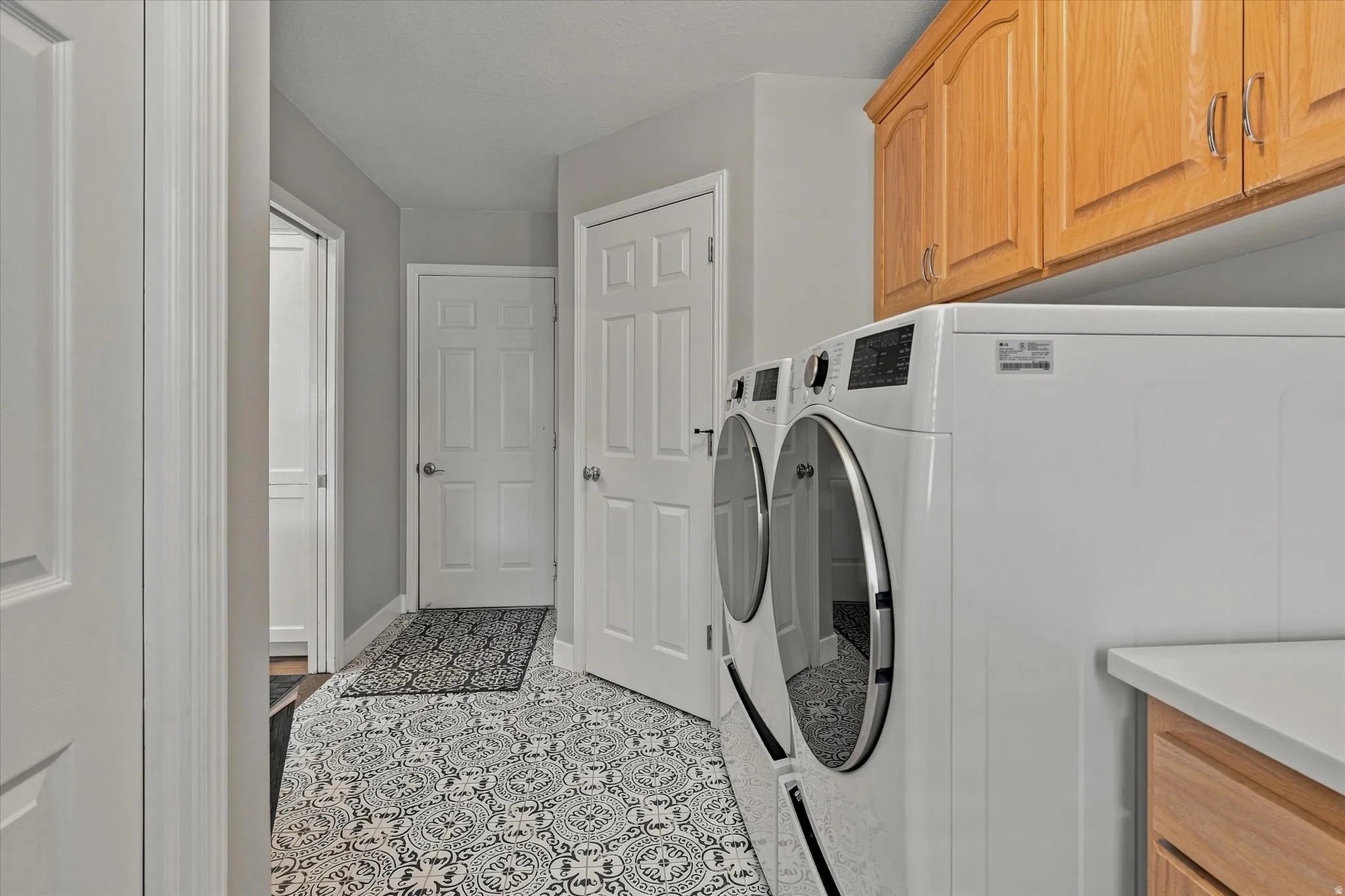 Laundry area featuring patterned tile flooring, wood cabinetry, and a countertop surface