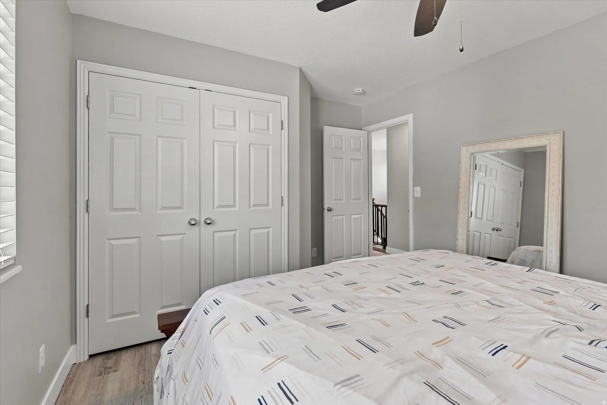 White paneled bi-fold closet doors, light gray wall paint, wood-finish flooring, white window blinds, and a ceiling fan