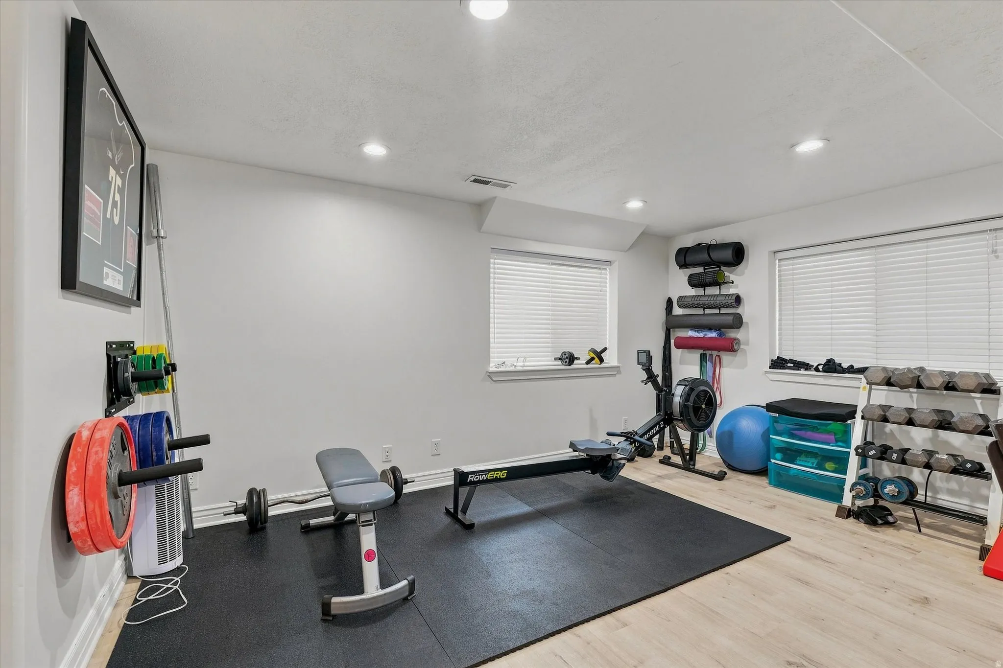 Recessed lighting illuminates the space, featuring light wood-finish flooring and multiple windows with blinds