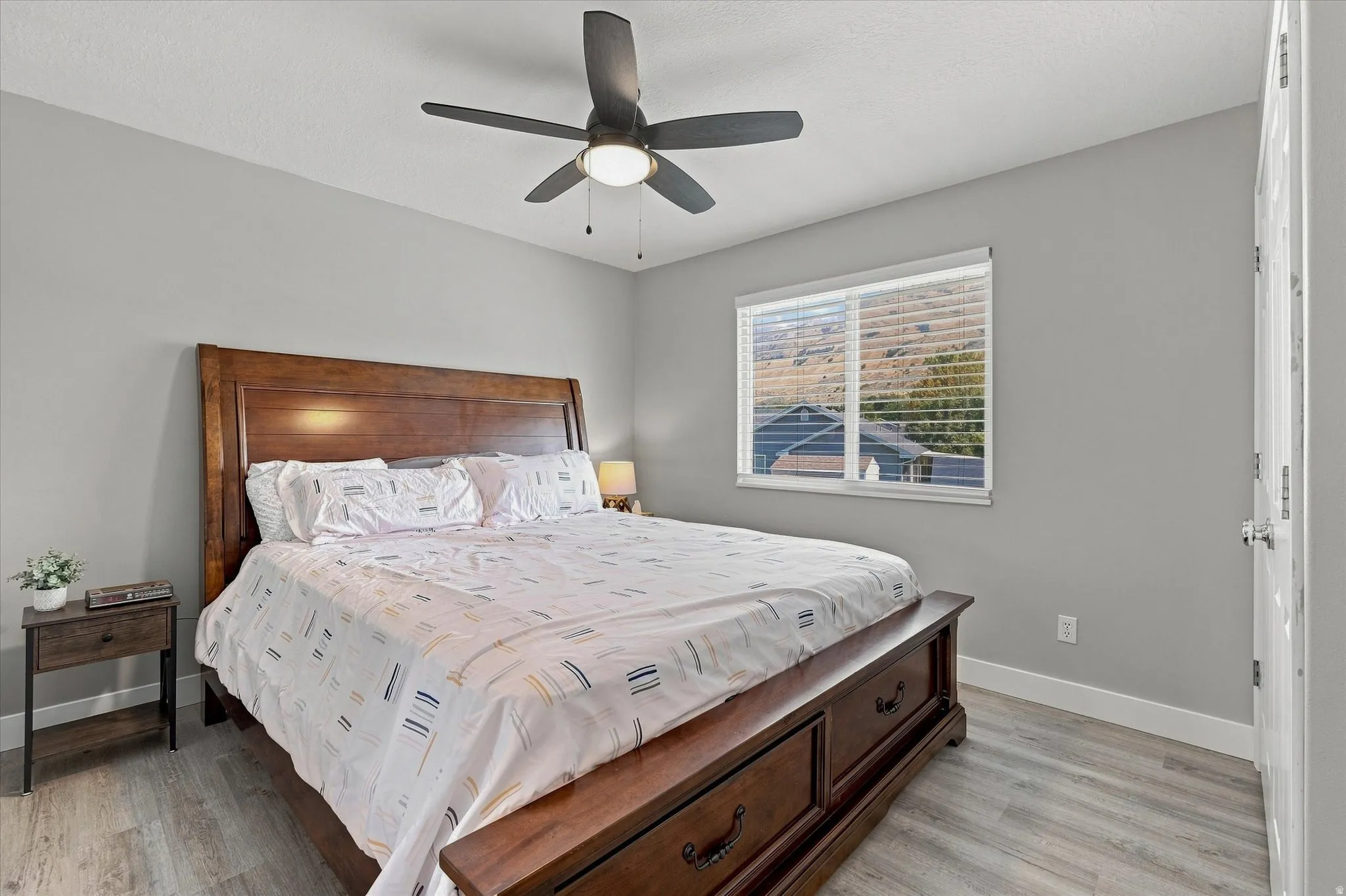 Light gray walls, wood-finish flooring, ceiling fan with integrated lighting, and a window with horizontal blinds
