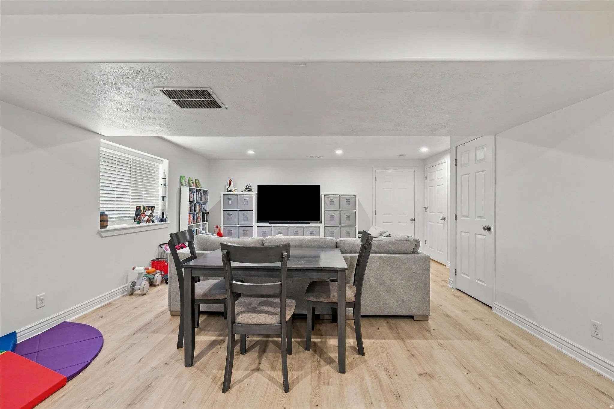 Recessed lighting, light wood-finish flooring, white paneled doors, and a window with blinds