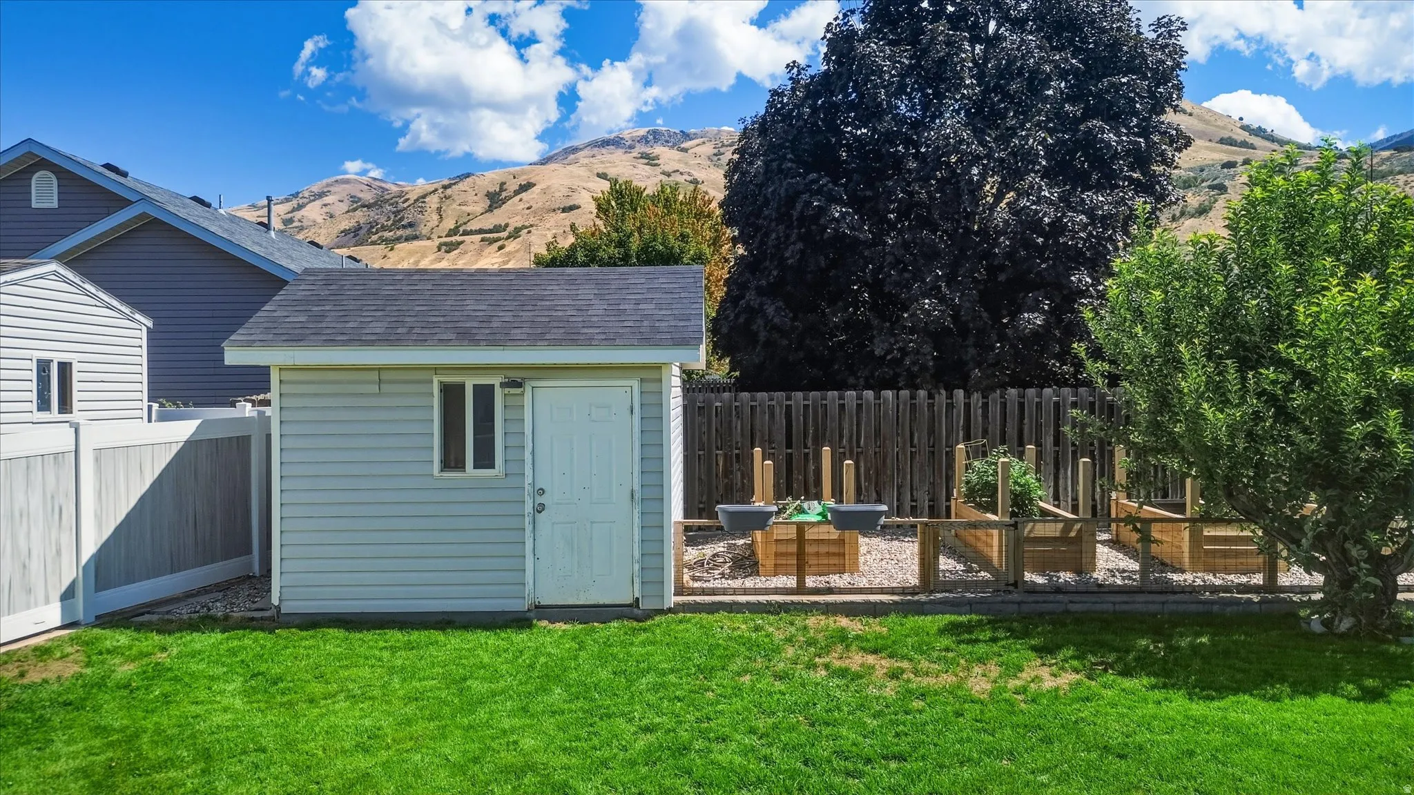 Expansive backyard featuring a storage shed, wood privacy fence, and multiple raised garden beds