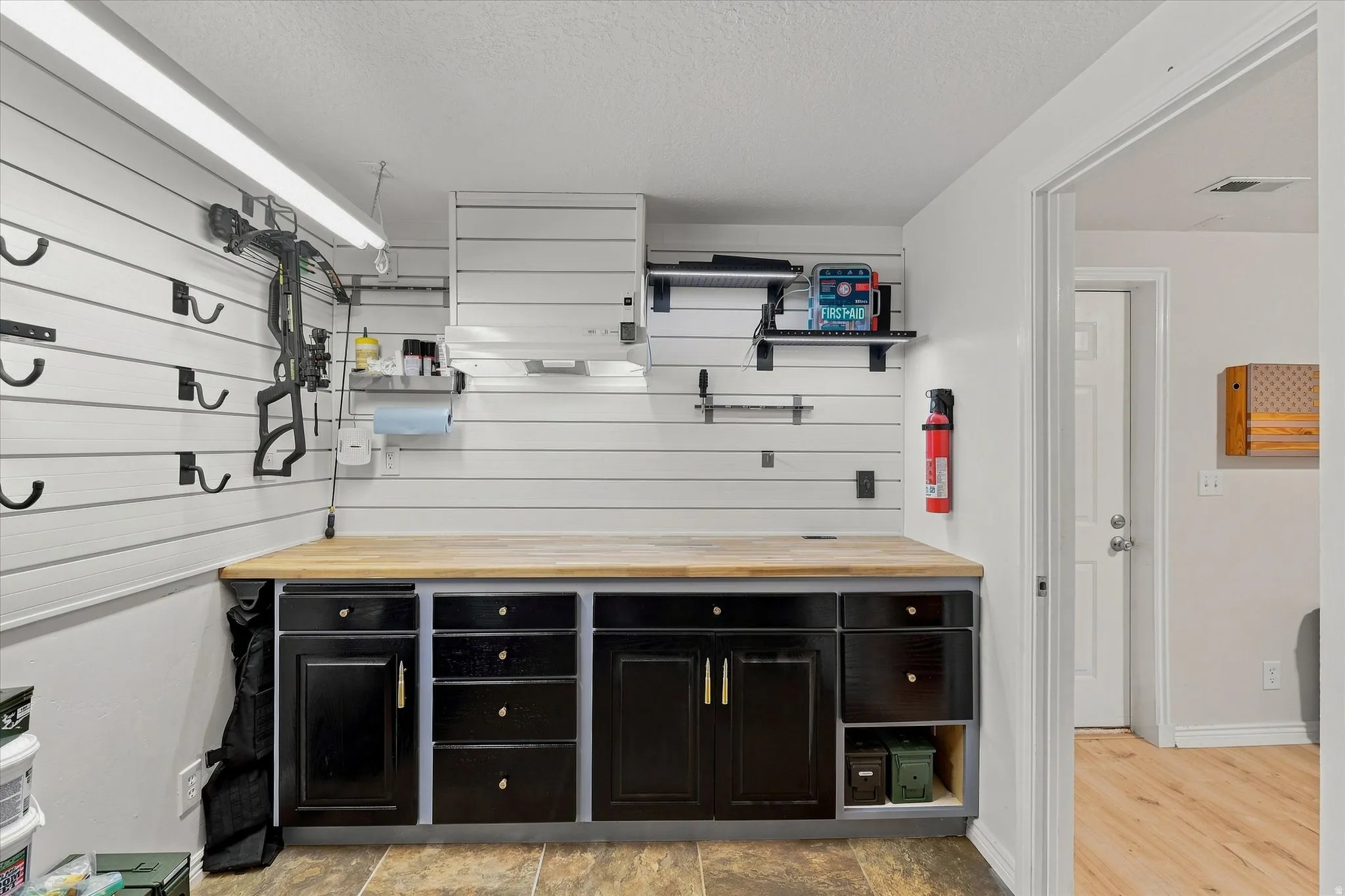 Built-in workbench with a wood-finish countertop, black cabinetry, and slat wall organization