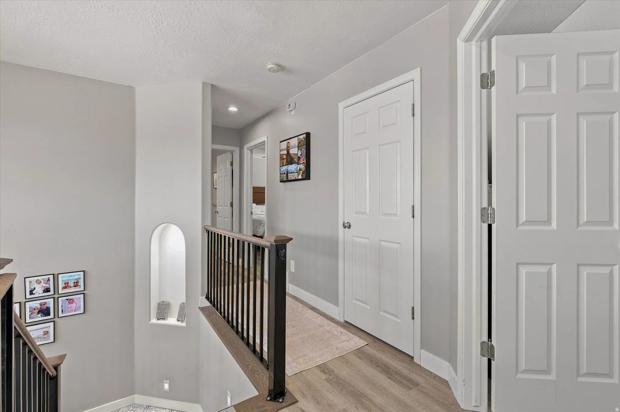 Upper landing with wood-finish flooring, recessed lighting, white paneled doors, and a built-in arched wall niche