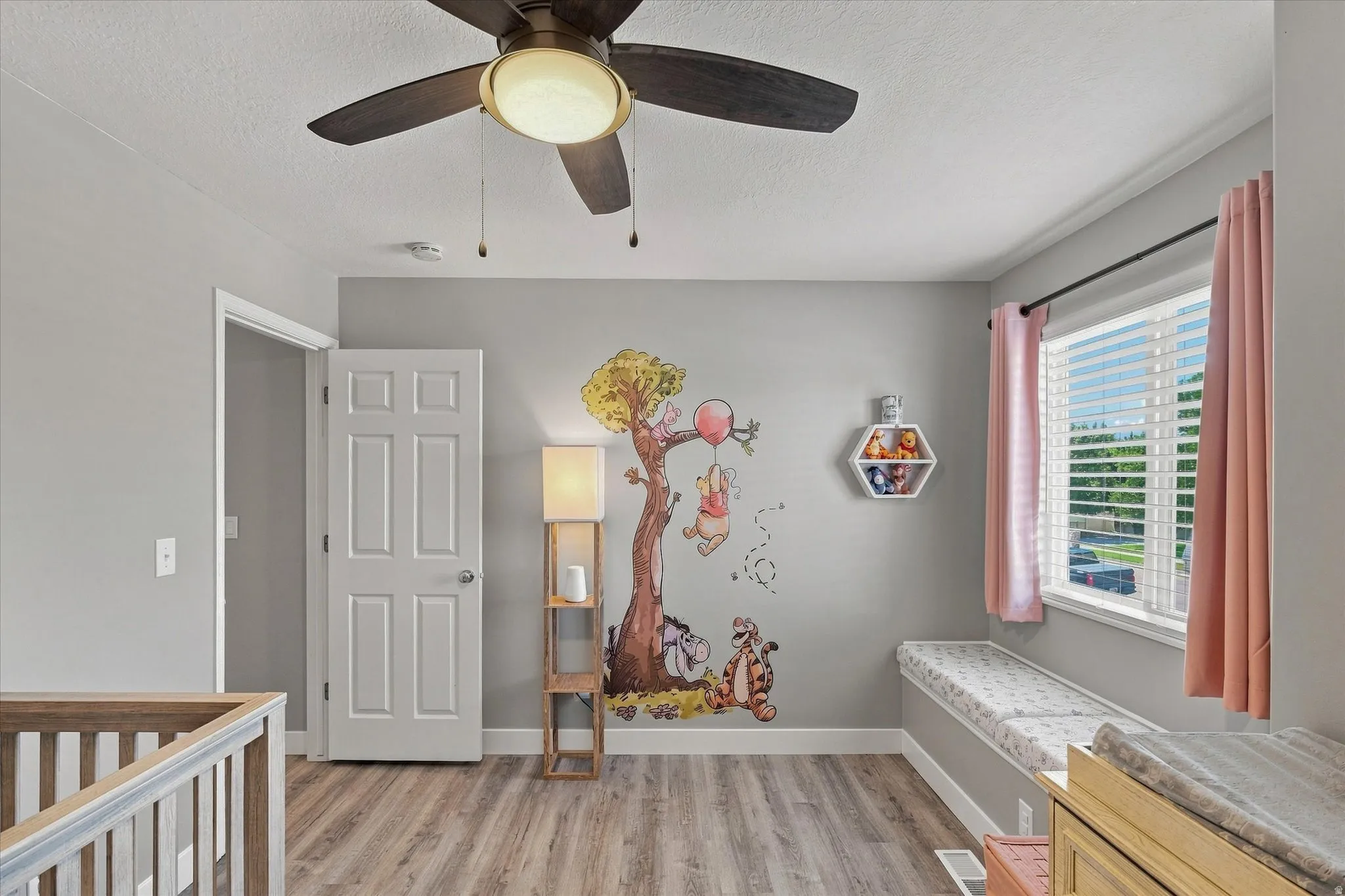 Wood-finish flooring, ceiling fan, natural light from a window with blinds, and a built-in window seat