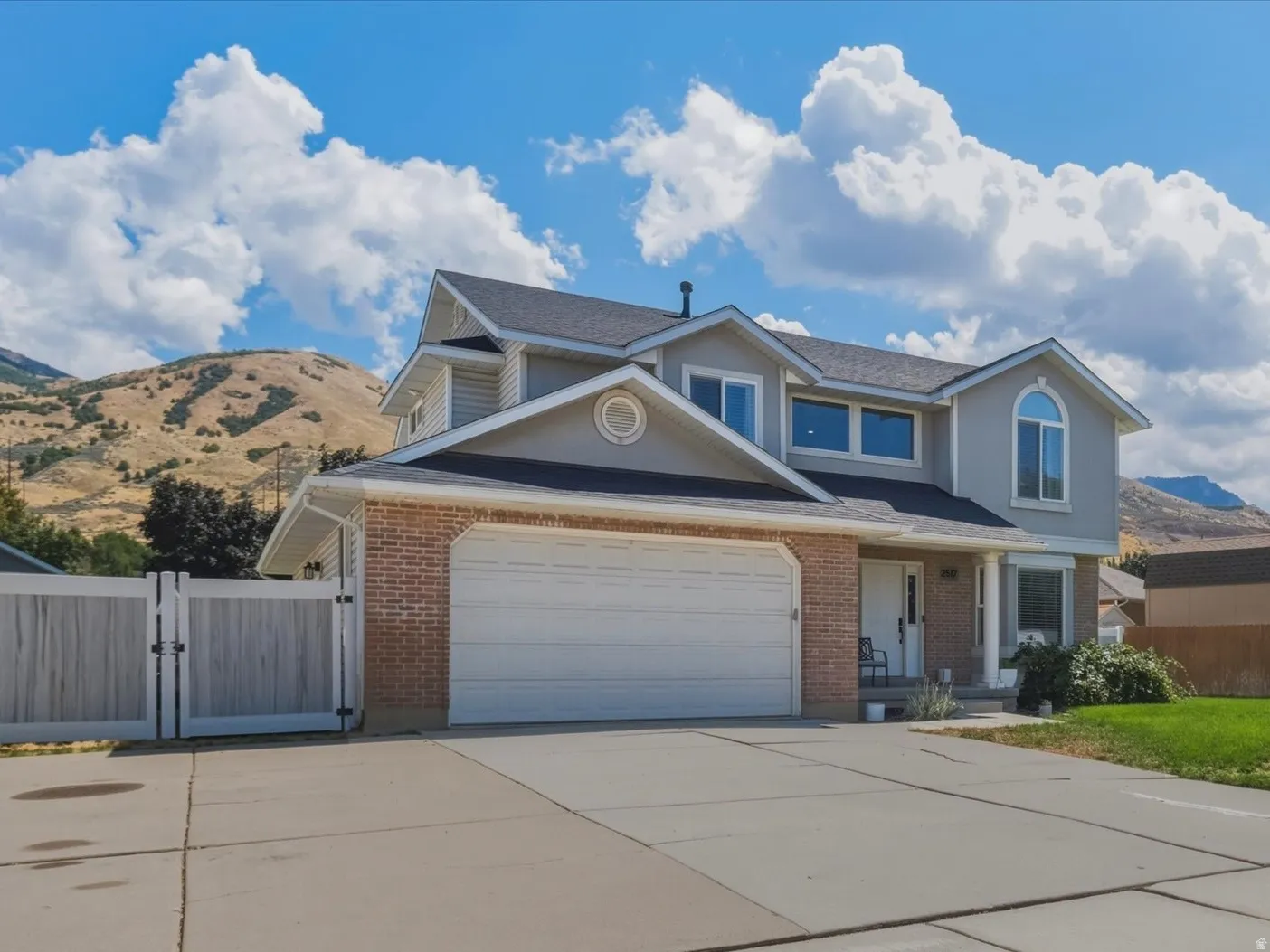 Two-story residence featuring brick and siding exterior, an attached garage, a wide paved driveway, and a fenced side yard