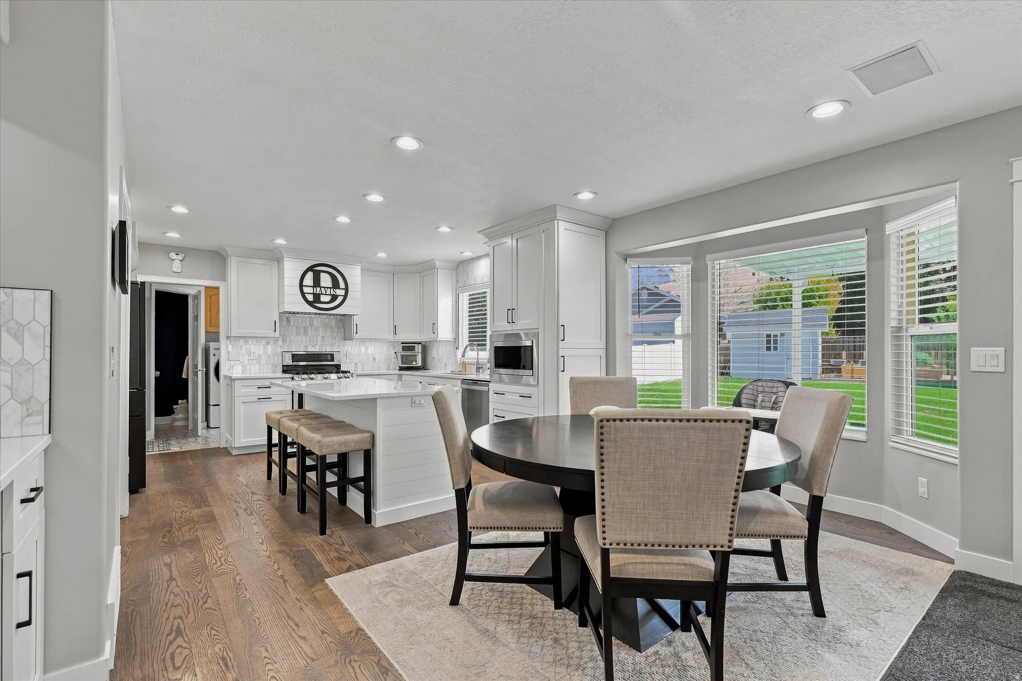 Open-concept kitchen and dining area featuring white cabinetry, stainless steel appliances, wood-finish flooring, recessed lighting, and glass sliding doors overlooking the landscaped yard