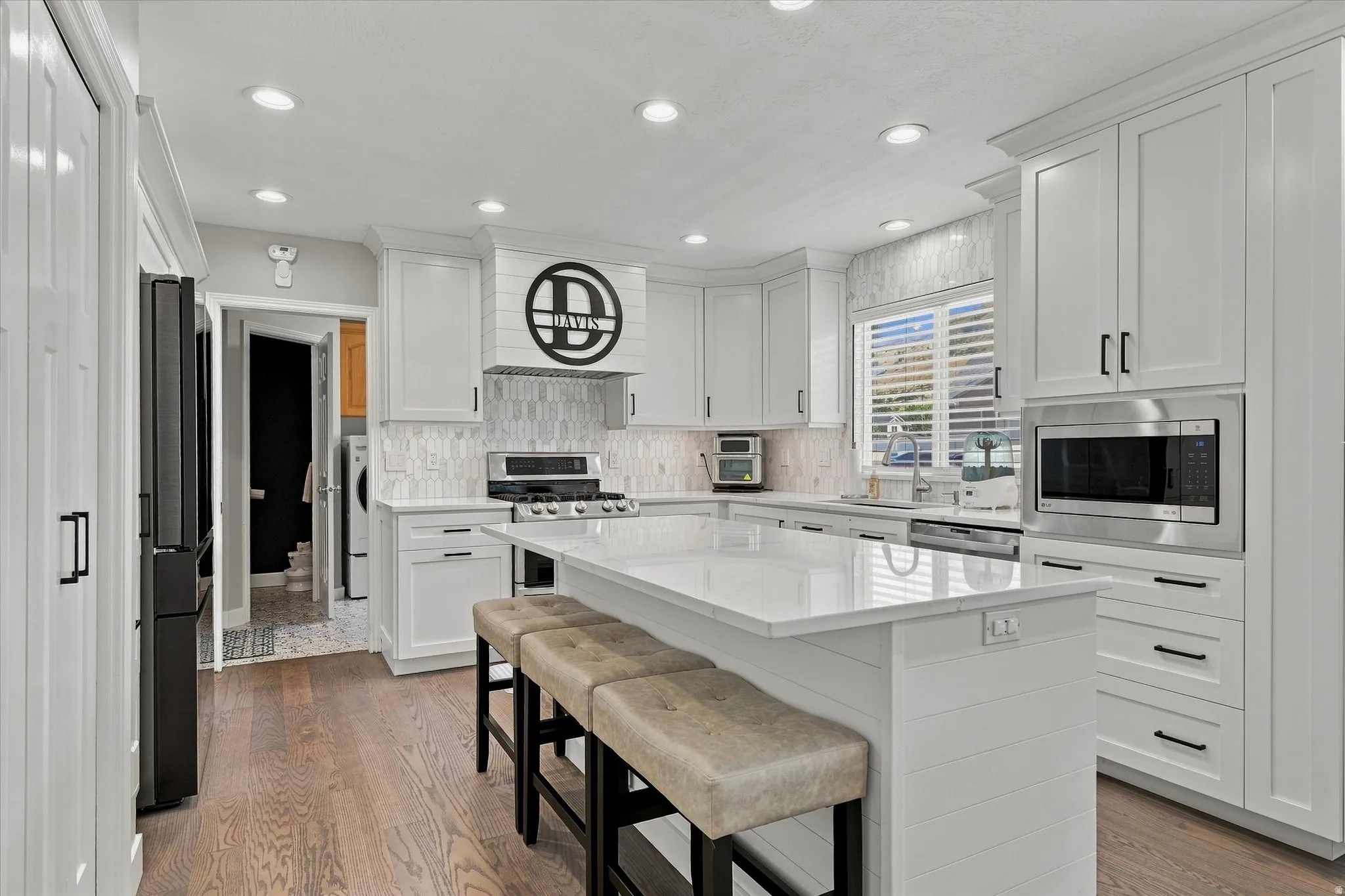 White shaker cabinetry with black hardware, white quartz countertops, stainless steel appliances, wood-finish flooring, and recessed lighting