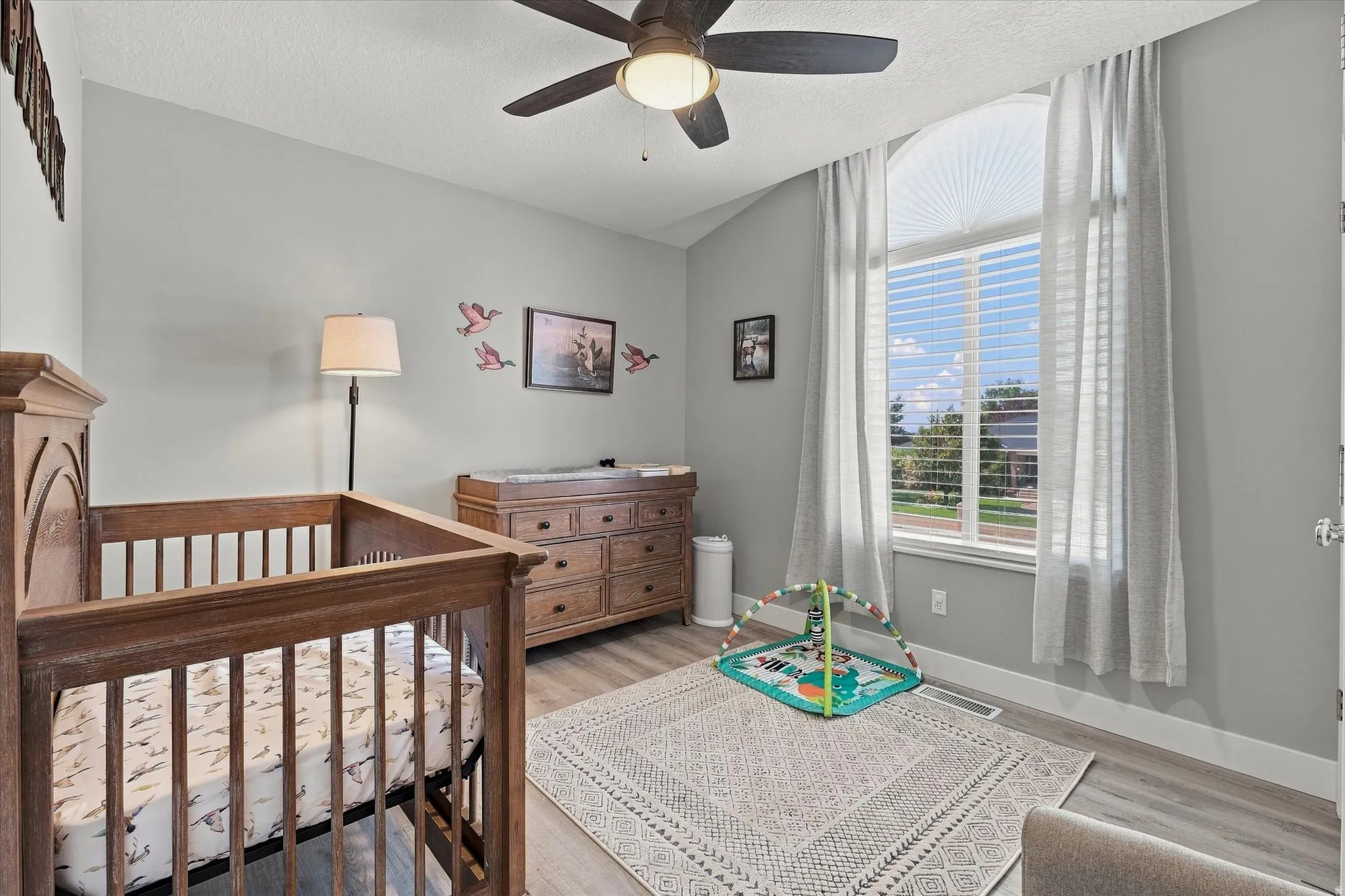 Vaulted ceiling with a ceiling fan, arched window with blinds, and wood-finish flooring