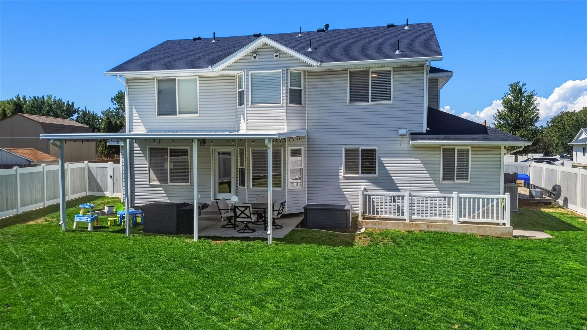 Expansive backyard featuring a covered patio, concrete pad, white vinyl fencing, and a durable asphalt shingle roof
