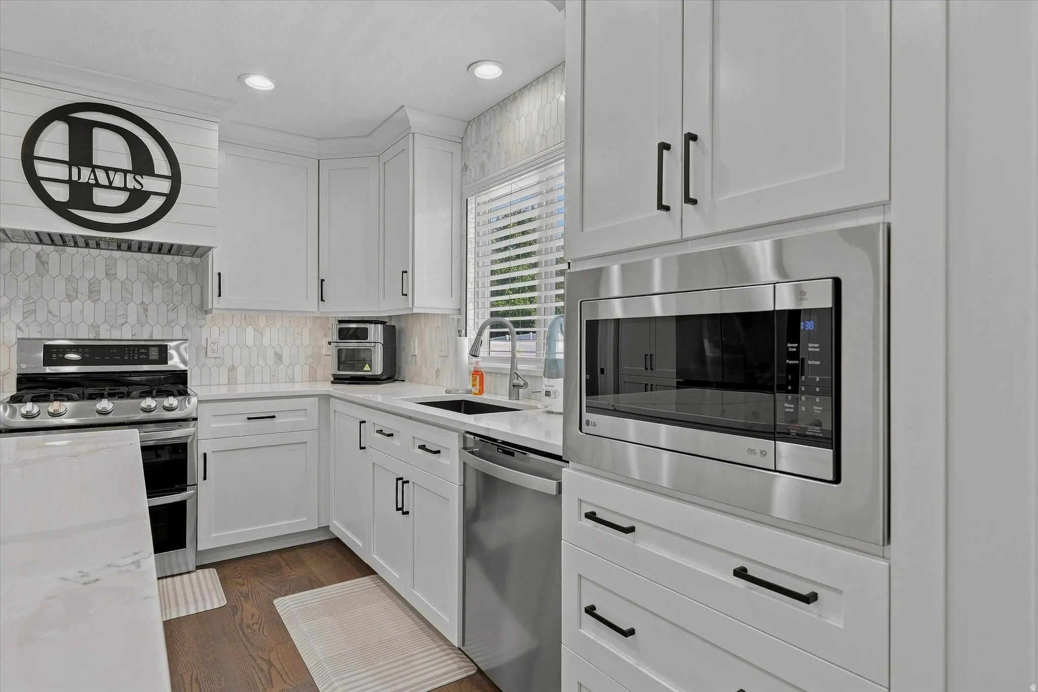 White shaker-style cabinetry with matte black hardware, stainless steel appliances, marble-look countertops, and a full-height tile backsplash