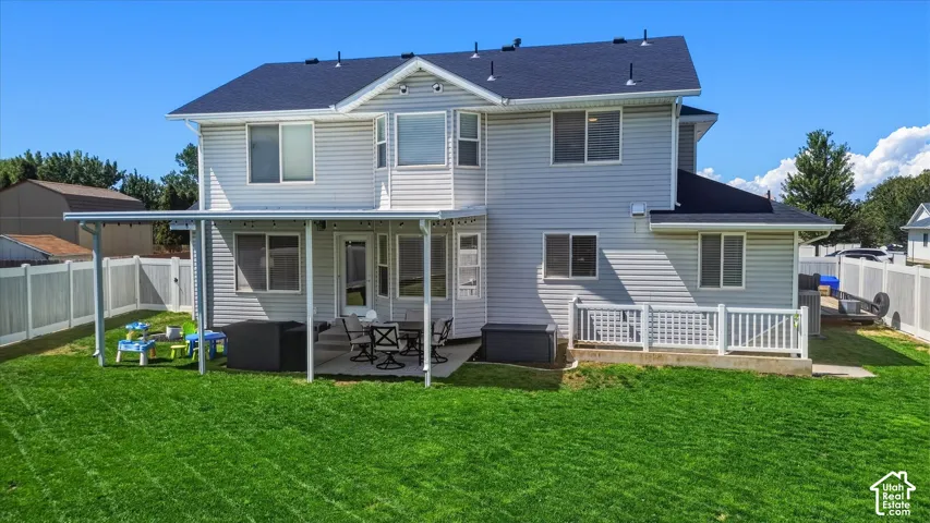 Expansive backyard featuring a covered patio, concrete pad, white vinyl fencing, and a durable asphalt shingle roof