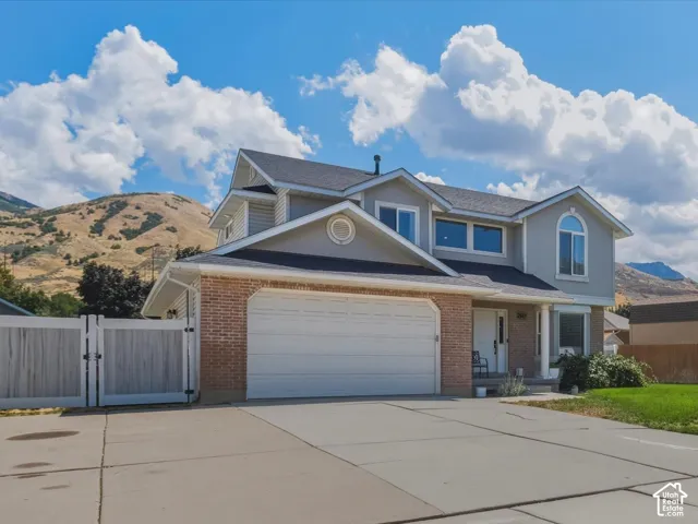 Two-story residence featuring brick and siding exterior, an attached garage, a wide paved driveway, and a fenced side yard