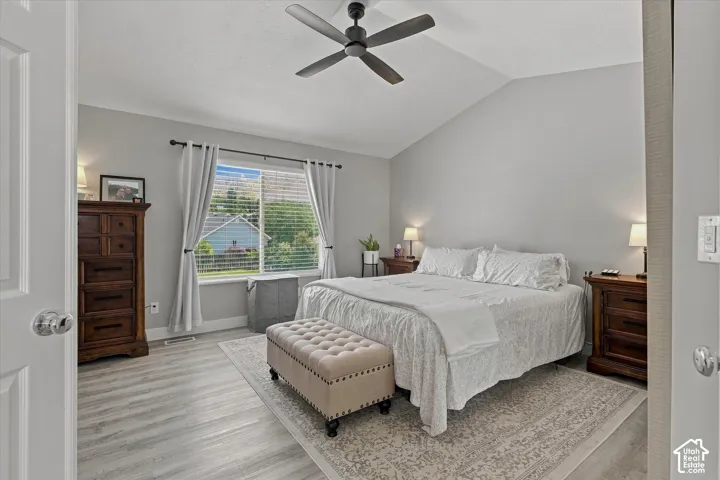 Vaulted ceiling, wood-finish flooring, ceiling fan, and a large window with blinds