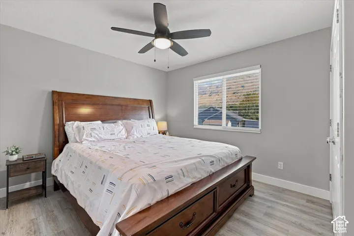Light gray walls, wood-finish flooring, ceiling fan with integrated lighting, and a window with horizontal blinds