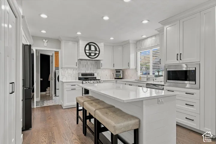 White shaker cabinetry with black hardware, white quartz countertops, stainless steel appliances, wood-finish flooring, and recessed lighting