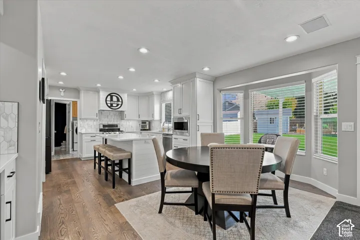 Open-concept kitchen and dining area featuring white cabinetry, stainless steel appliances, wood-finish flooring, recessed lighting, and glass sliding doors overlooking the landscaped yard