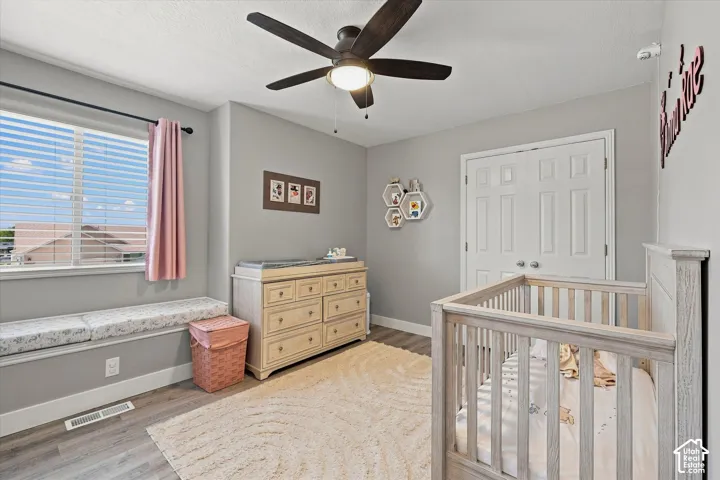 Window bench seating, wood-finish flooring, ceiling fan with light fixture, and double-door closet