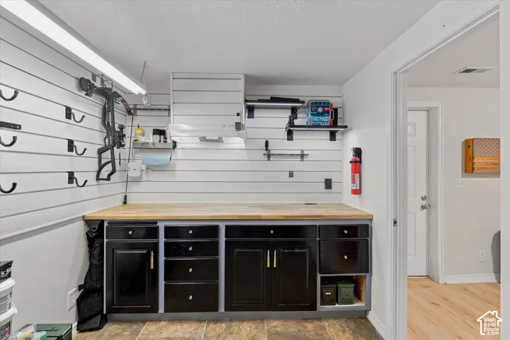 Built-in workbench with a wood-finish countertop, black cabinetry, and slat wall organization