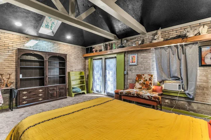 Vaulted ceiling with exposed beams, brick accent walls, skylight, and built-in shelving unit