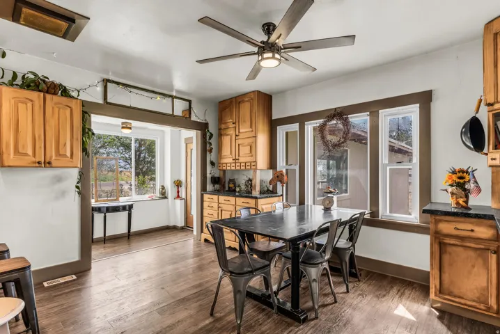 Wood-finish flooring, wood cabinetry with dark countertops, a ceiling fan with integrated lighting, and multiple windows providing natural illumination