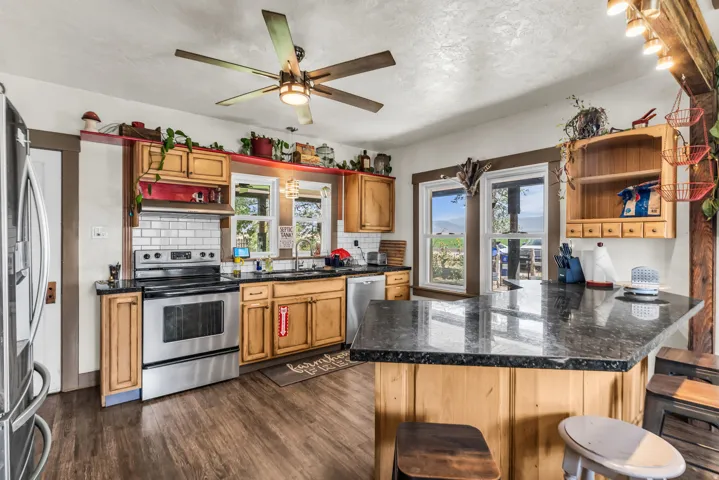 Kitchen featuring wood-finish cabinetry, stainless steel appliances, dark stone countertops, wood-finish flooring, and a ceiling fan