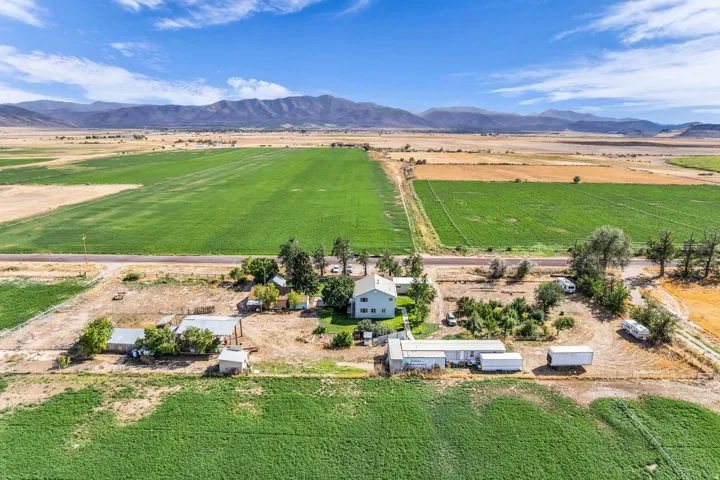 Expansive agricultural land with a single-family residence, multiple outbuildings, and mountain scenery