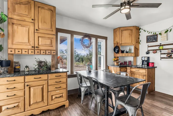 Wood-finish flooring, natural wood cabinetry with dark hardware, dark countertops, multiple windows, and a ceiling fan with integrated lighting