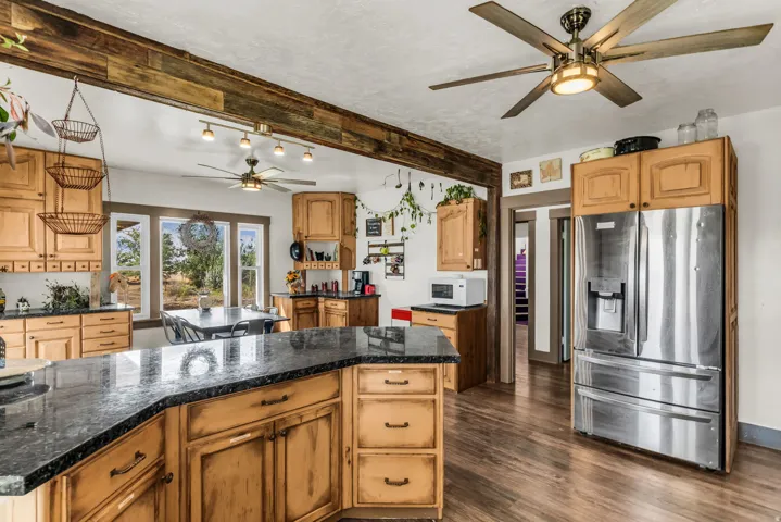Spacious kitchen featuring wood-finish flooring, custom wood cabinetry, dark countertops, and a stainless steel refrigerator
