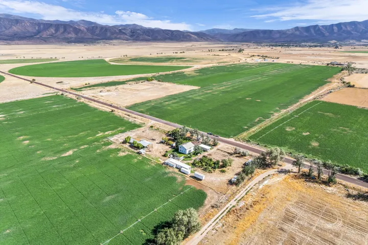 Expansive agricultural property featuring cultivated fields, irrigation systems, multiple outbuildings, established trees, and a distant mountain range backdrop