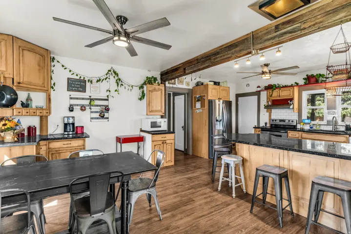 Light wood-finish cabinetry, dark countertops, wood-finish flooring, and exposed wood beam