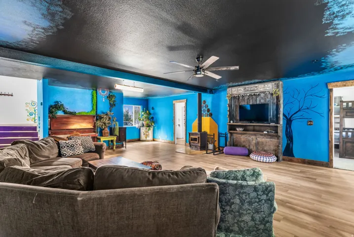 Wood-finish flooring throughout, ceiling fan, brightly colored walls, built-in media console, and a corner fireplace