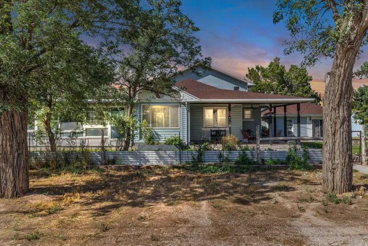 Light blue siding exterior with a covered porch, brown roof, and mature trees