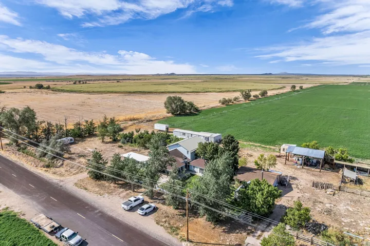 Expansive rural property featuring a main residence, secondary structures, a covered outbuilding, and significant green acreage
