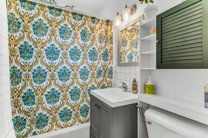White subway tile walls, gray vanity with integrated sink, wall-mounted medicine cabinet with mirror, built-in shelving, and a louvered cabinet door