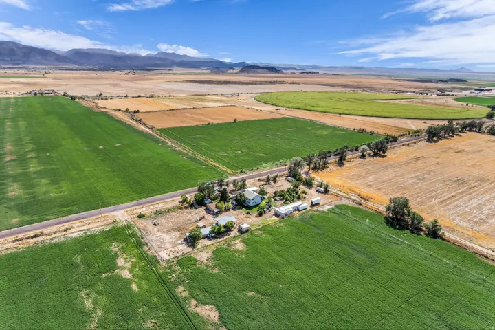 Expansive agricultural property featuring cultivated fields, a central building cluster, and distant mountain ranges