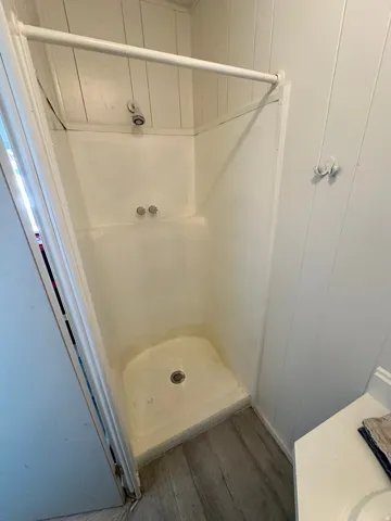 Compact shower stall with a white base and integrated walls, complemented by wood-finish flooring