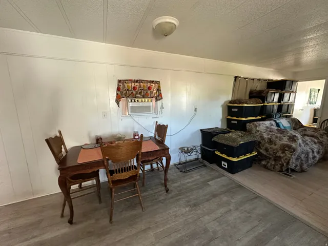 Window-mounted air conditioning unit, light wood-finish flooring, white paneled walls, and ceiling light fixture