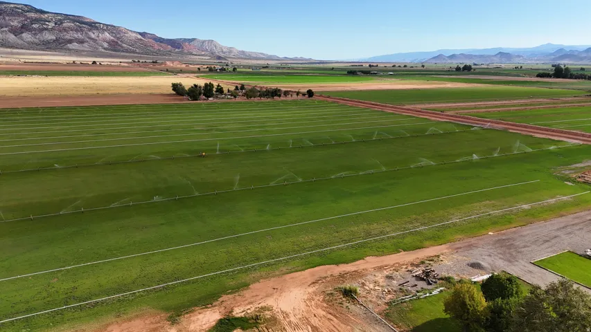 Expansive green fields with active irrigation systems, bordered by natural terrain and distant mountains