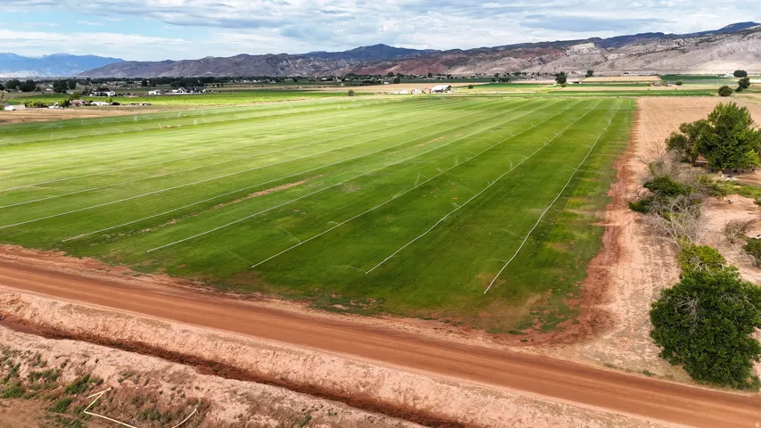 Expansive agricultural land featuring a verdant field with irrigation lines, bordered by a dirt road and distant mountains