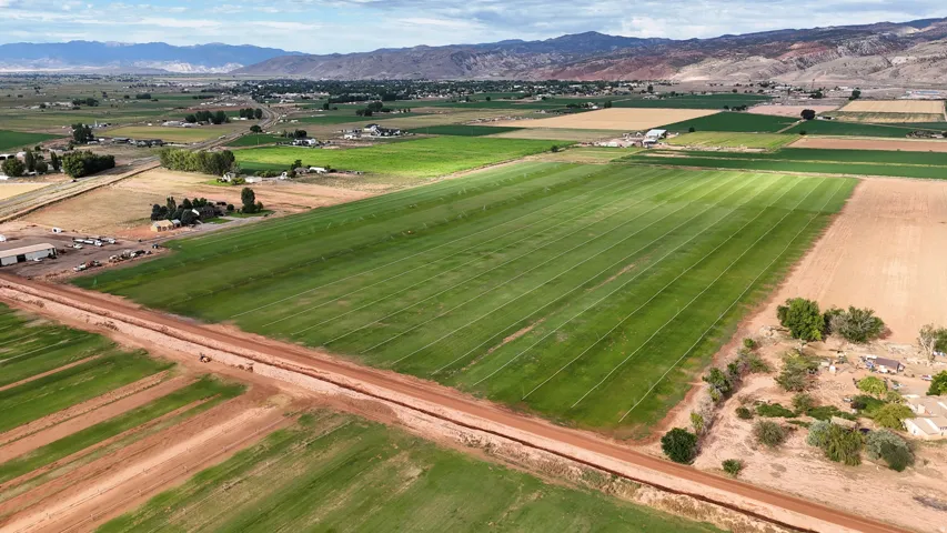 Expansive agricultural land featuring cultivated fields, distant mountainous terrain, and a visible dirt road