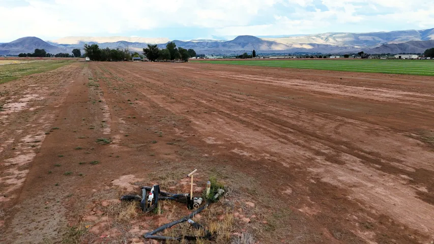 Expansive open field with cultivated land, featuring a verdant field in the distance and a mountainous backdrop
