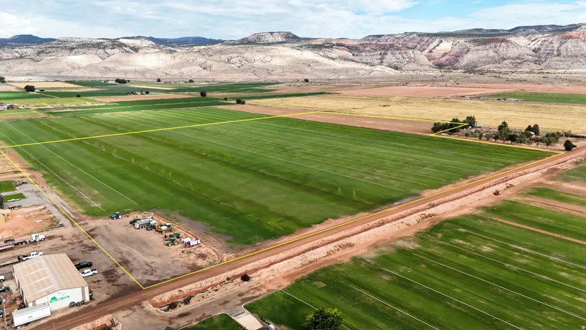 Expansive agricultural land featuring cultivated fields, a large industrial building, and a dirt road