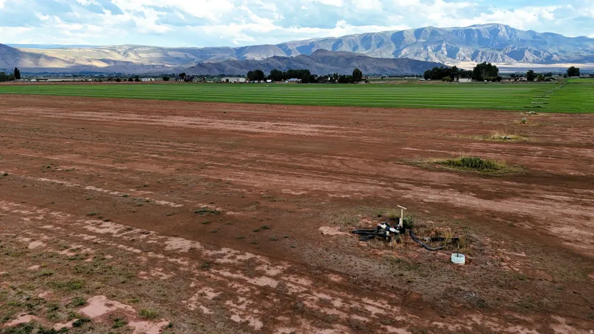 Expansive land featuring a pump system, cultivated fields, and distant mountain ranges