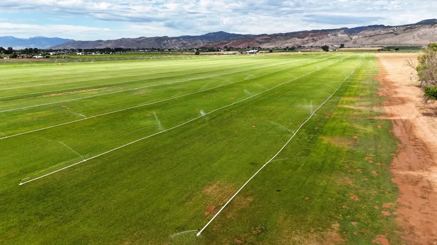 Expansive green field with visible irrigation lines, bordered by a natural landscape