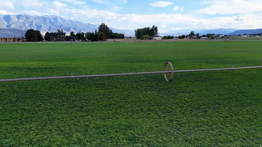 Expansive green field with a distant mountain range and scattered residential structures